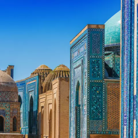Islamic architectural complex with domed and arched structures covered in turquoise and blue patterned tiles under a clear blue sky